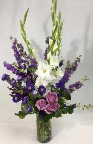shades of purple using larkspur, Matsumoto asters, standard roses, and stock with white gladiolas and salal in a tall cylinder vase